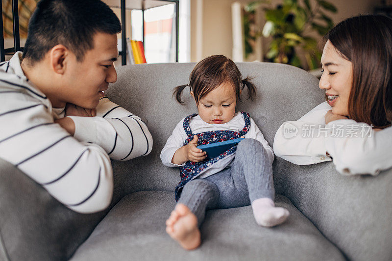 Mother and father looking at their daughter while she is using smart phone on the sofa